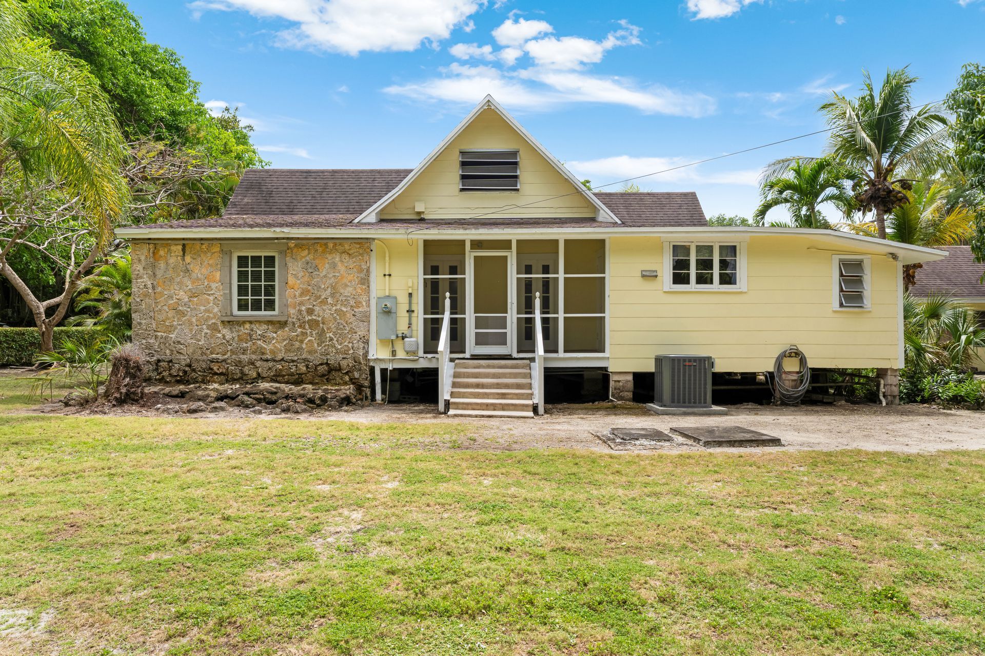 Yellow single-story house with a front porch, surrounded by a grassy yard and trees under a blue sky