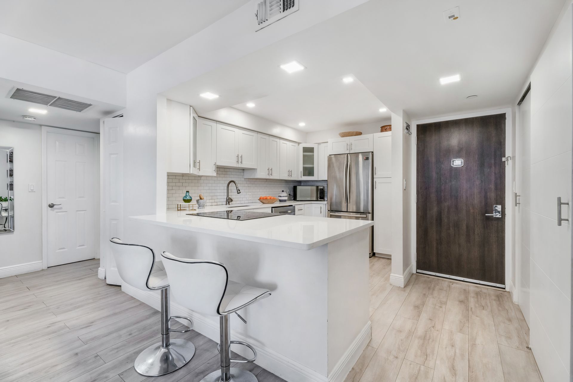 Bright white modern kitchen with island, bar stools, stainless fridge, and wood-look flooring