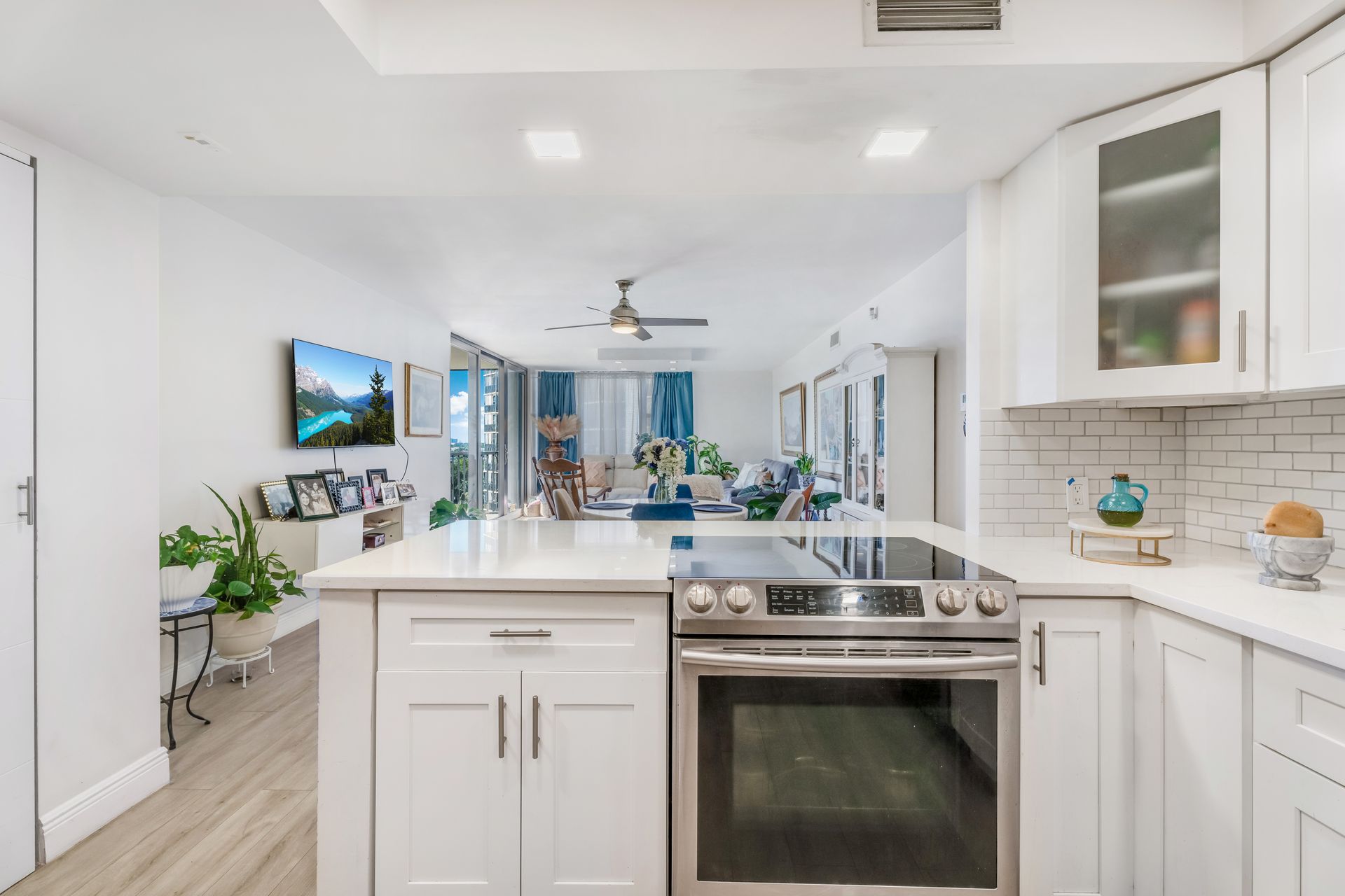 Bright white kitchen with island, stainless stove, wall TV, and open view to living area