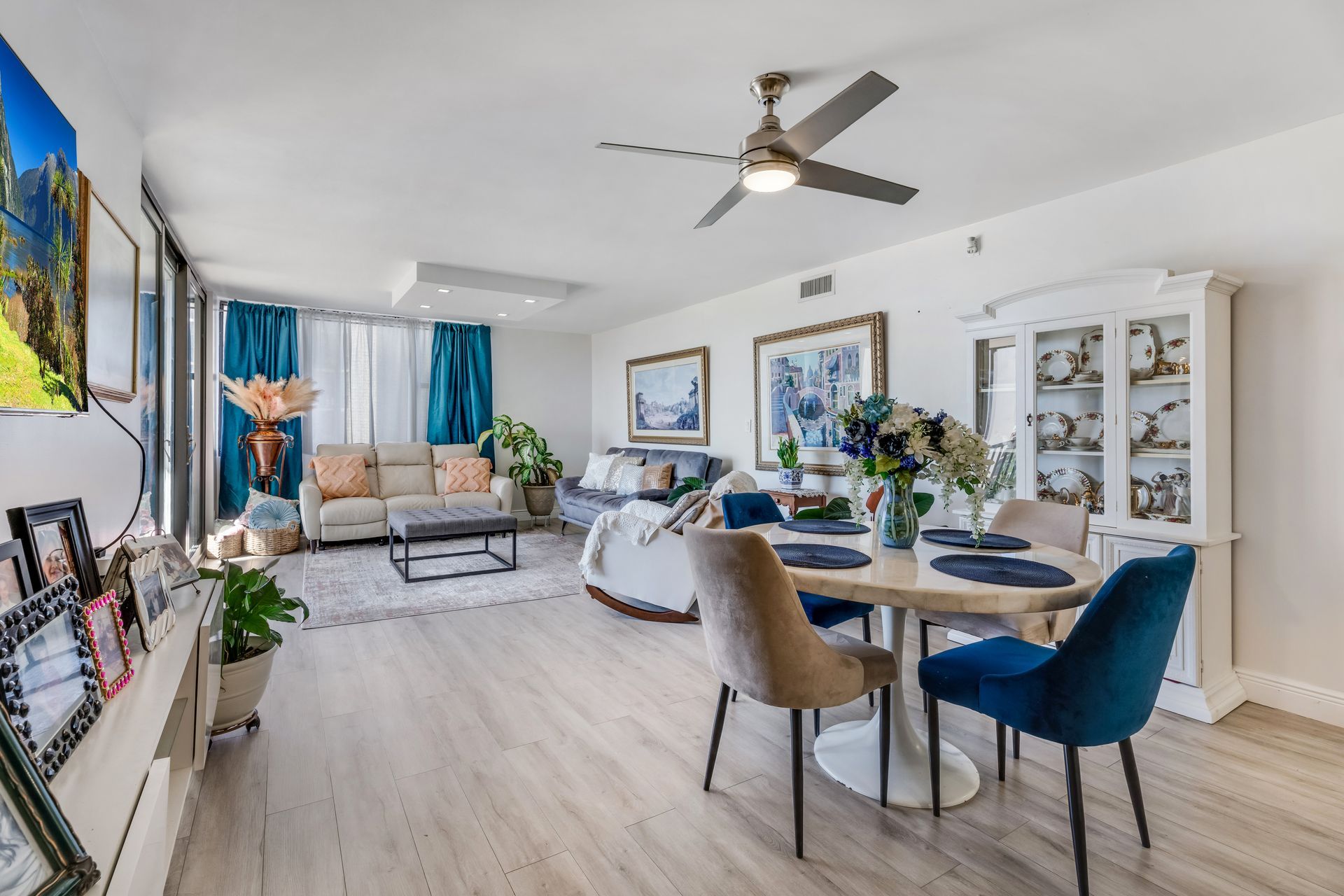 Bright modern living room with dining table, blue accents, and large TV mounted on the wall