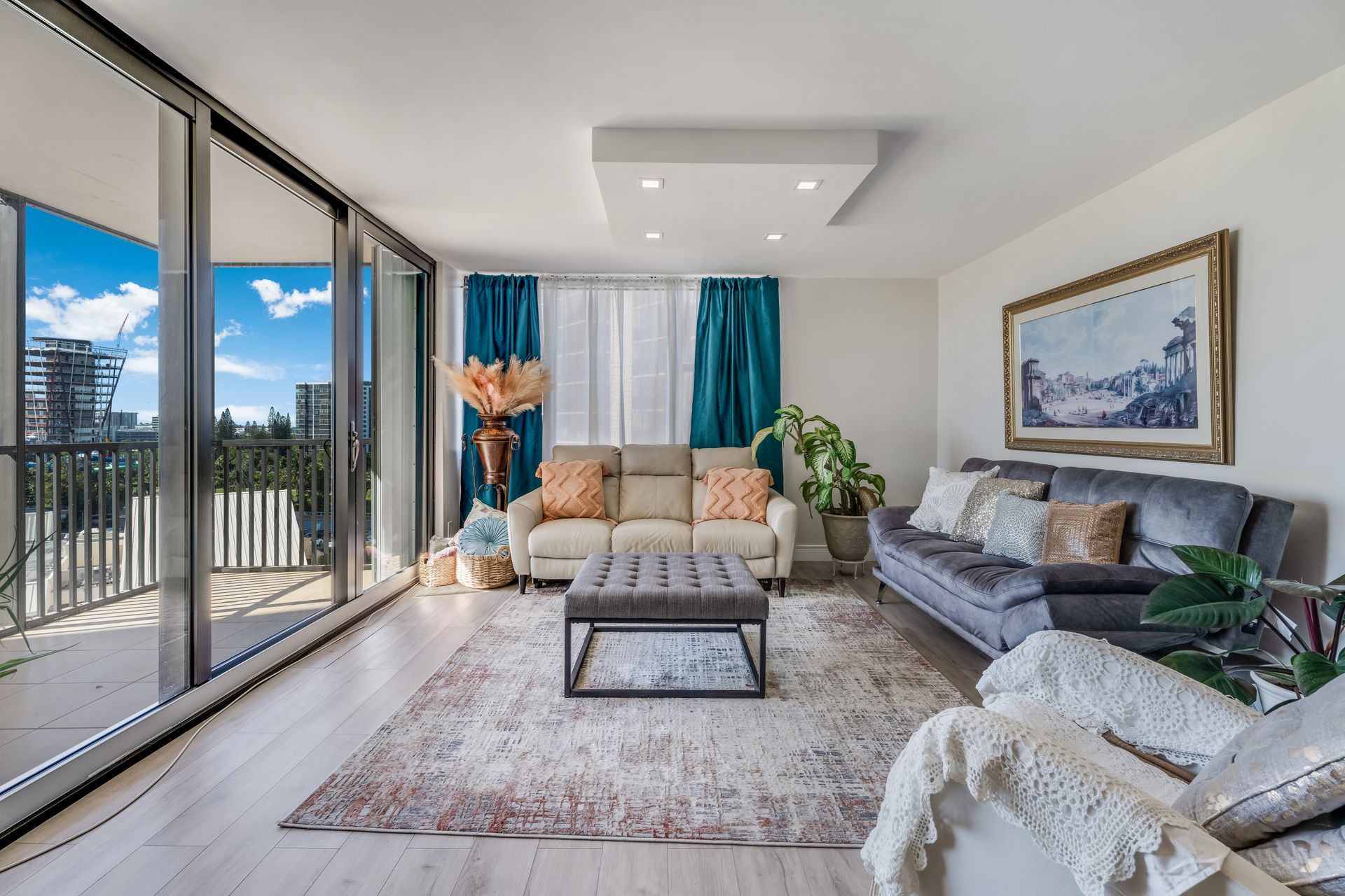 Bright modern living room with large windows, gray sofa, beige chair, and a view of balconies outside