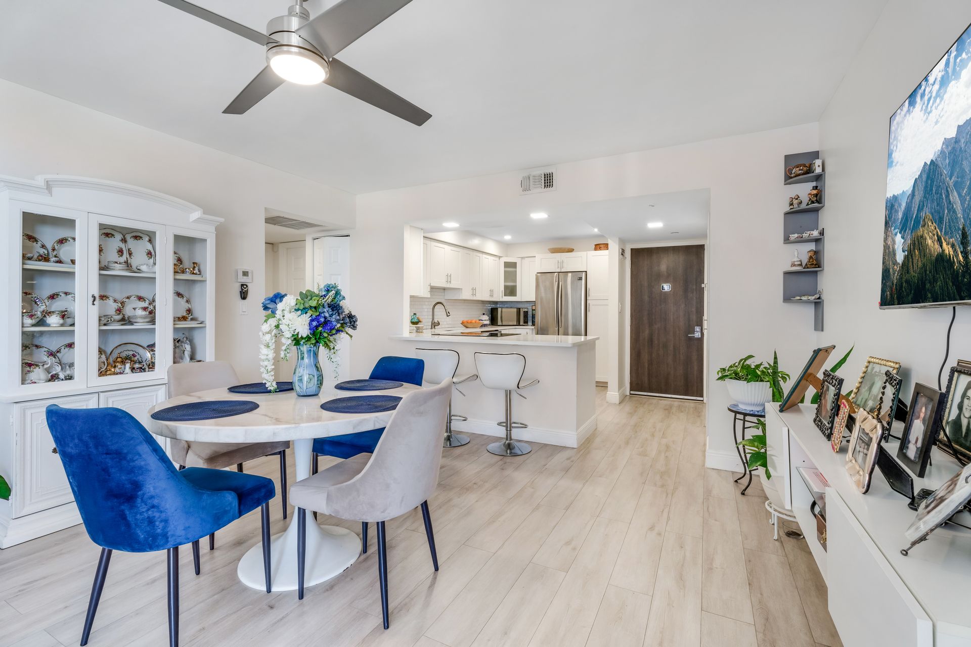 Bright open dining room and kitchen with blue chairs, white decor, and light wood floors