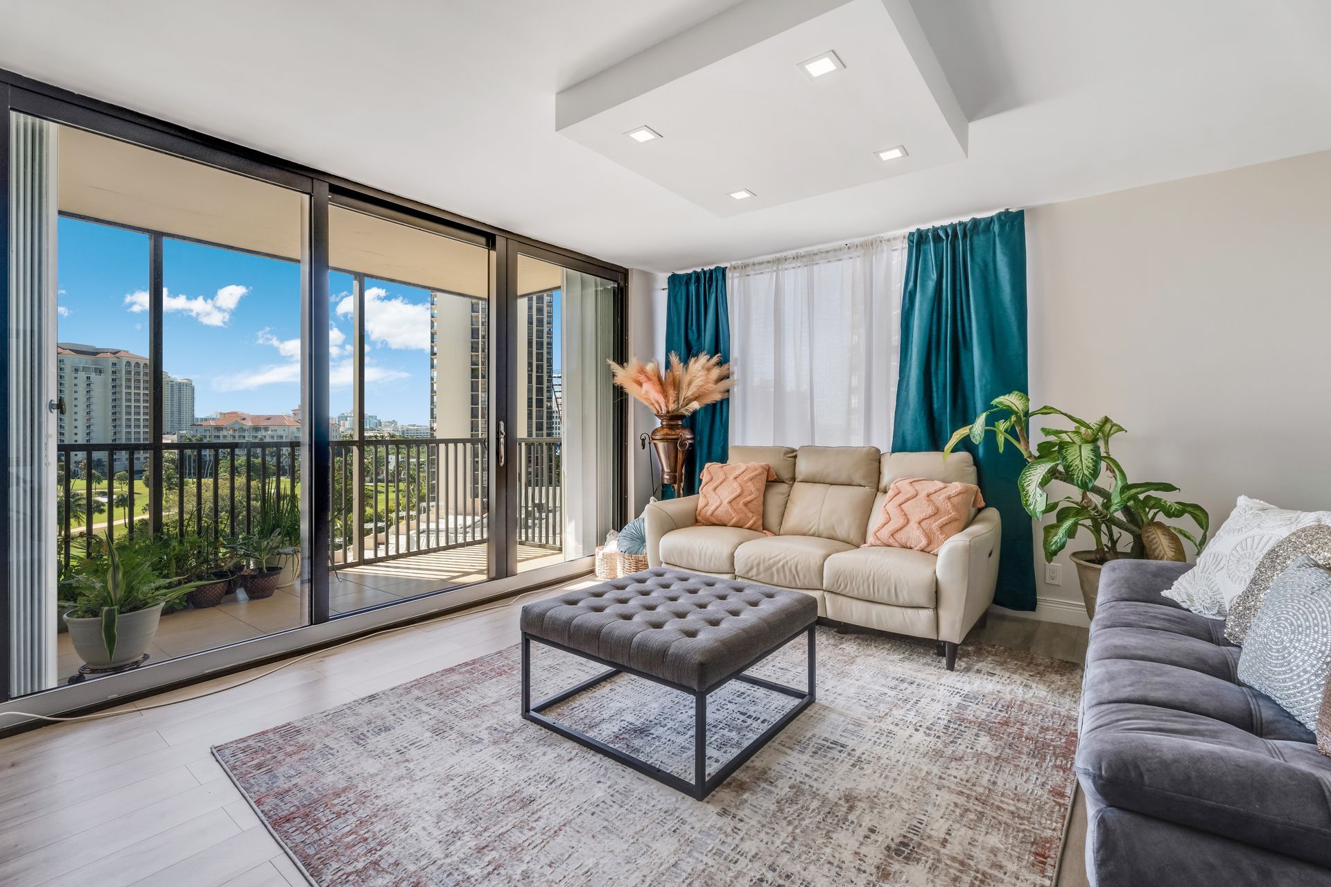 Bright modern living room with sectional sofa, coffee table, rug, large windows, and balcony view