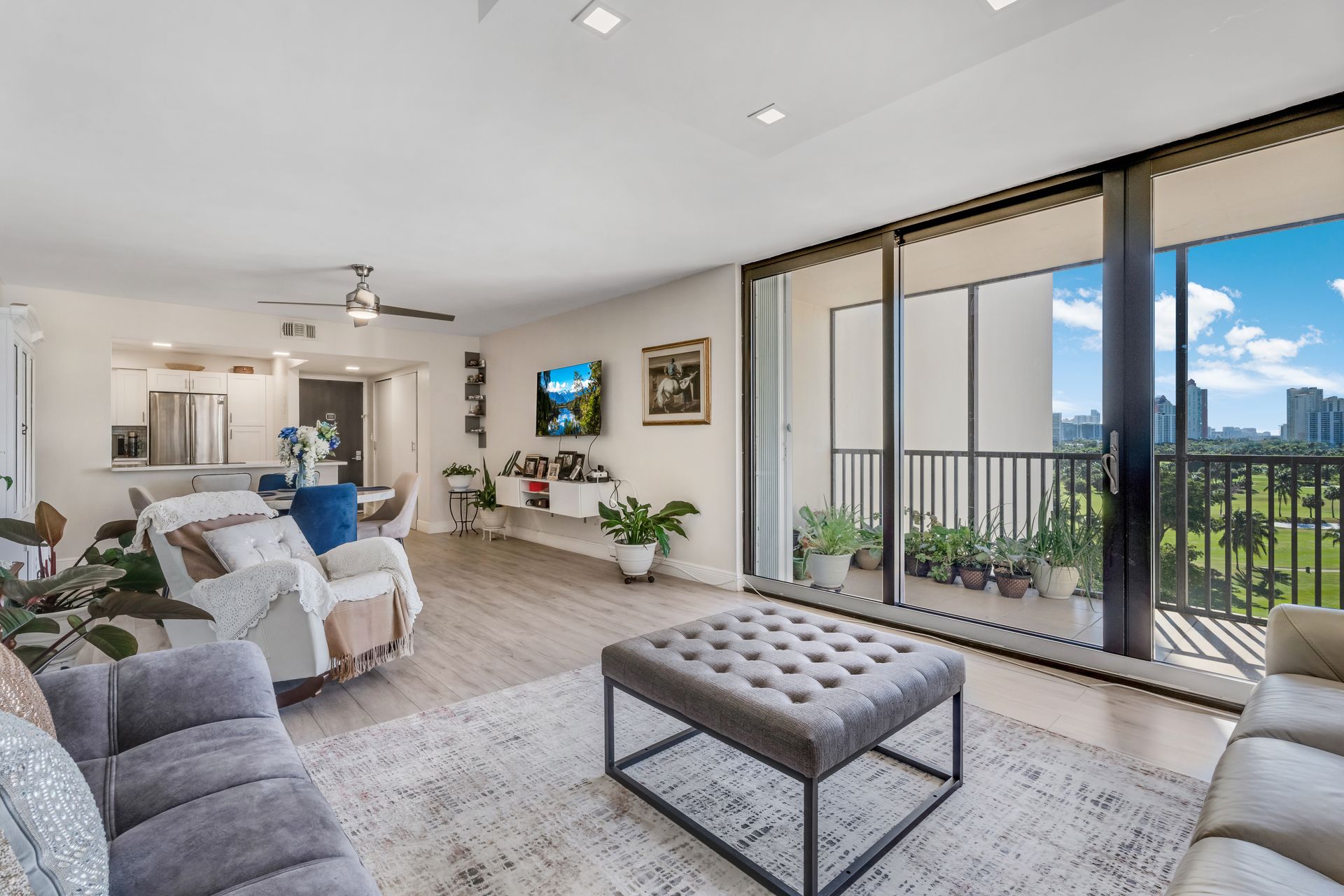Bright modern living room with gray sofa, tufted ottoman, and large sliding glass doors to a balcony.