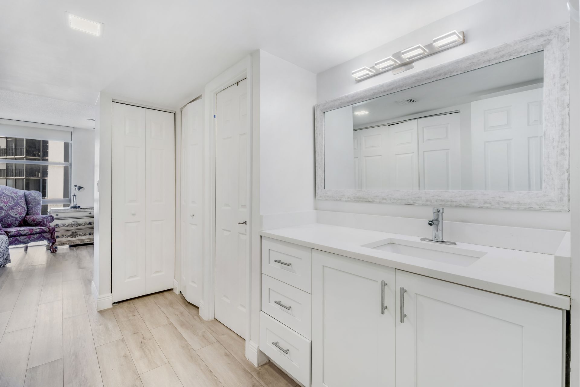 Bright white bathroom vanity with large mirror and built-in closets in a modern interior