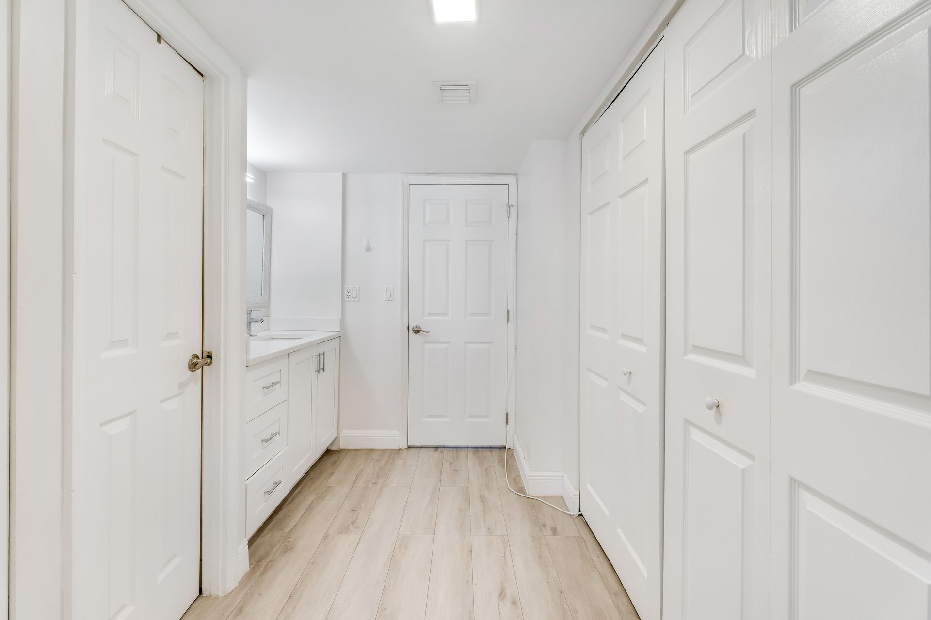 Bright white hallway with paneled doors, light wood floors, and a vanity on the left