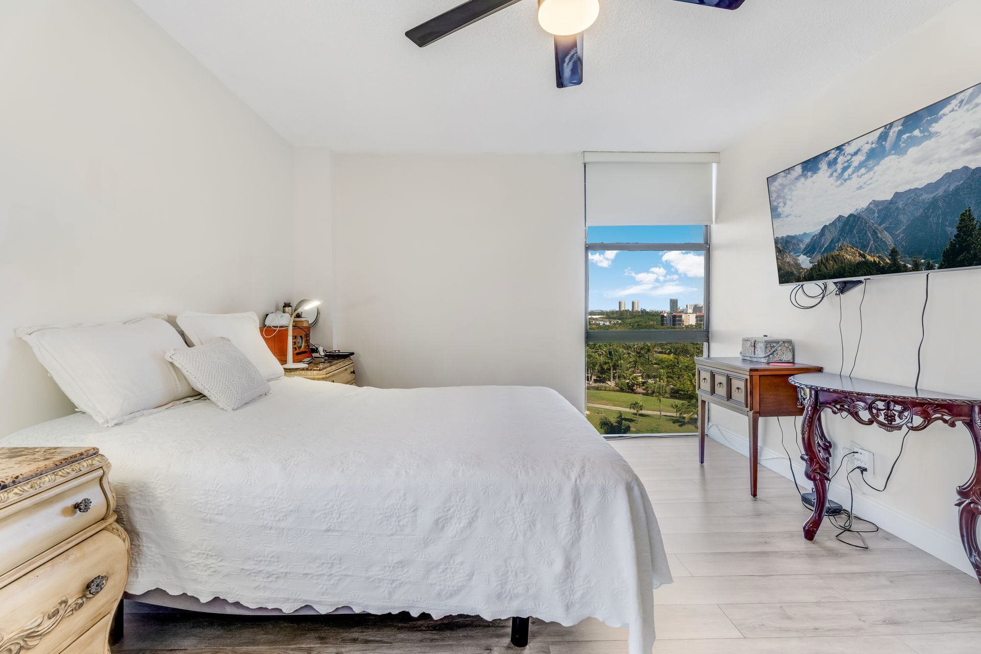 Bright bedroom with white bedding, ocean view window, and mountain wall art