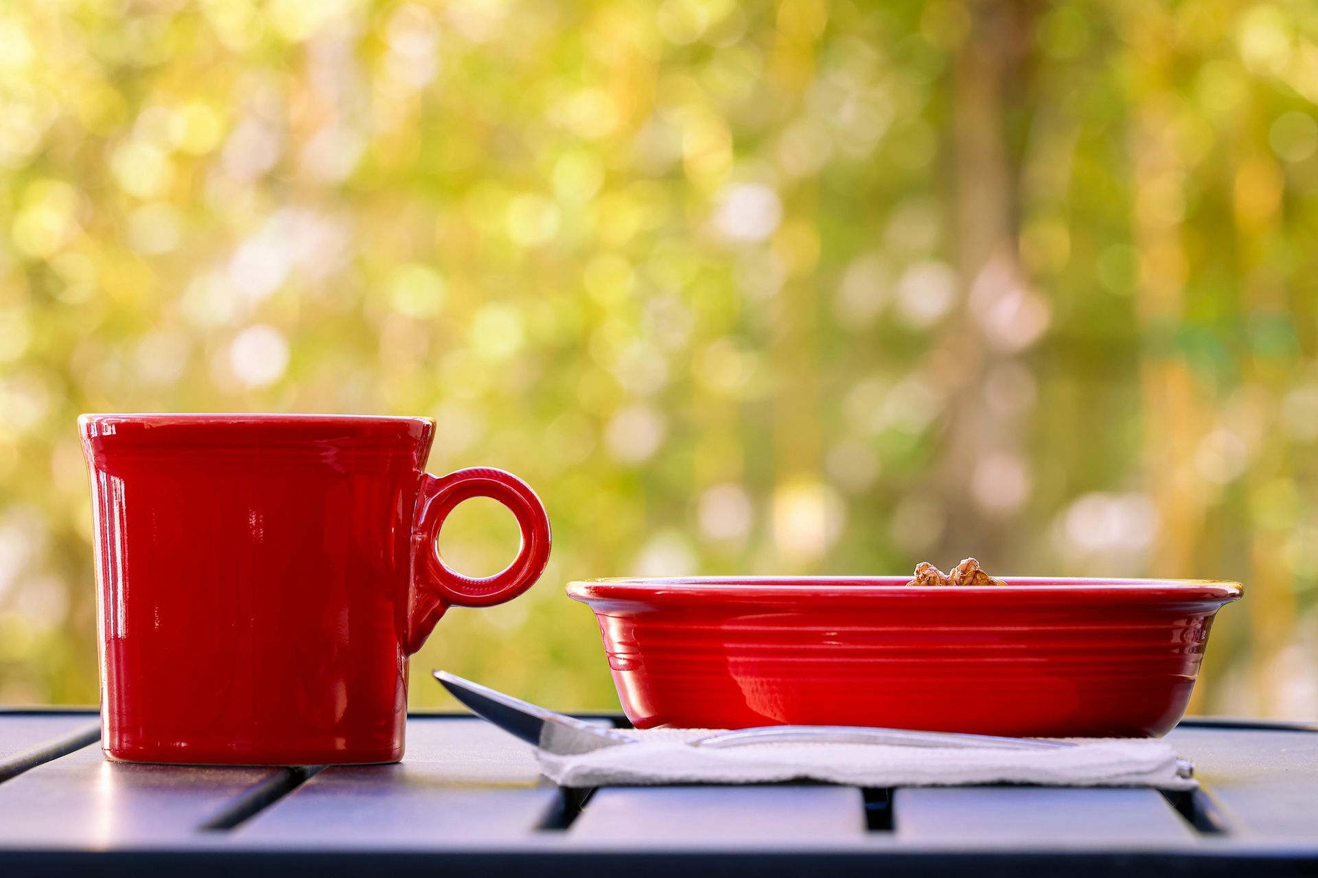 Red mug and red bowl on a tray against a blurred yellow-green background.