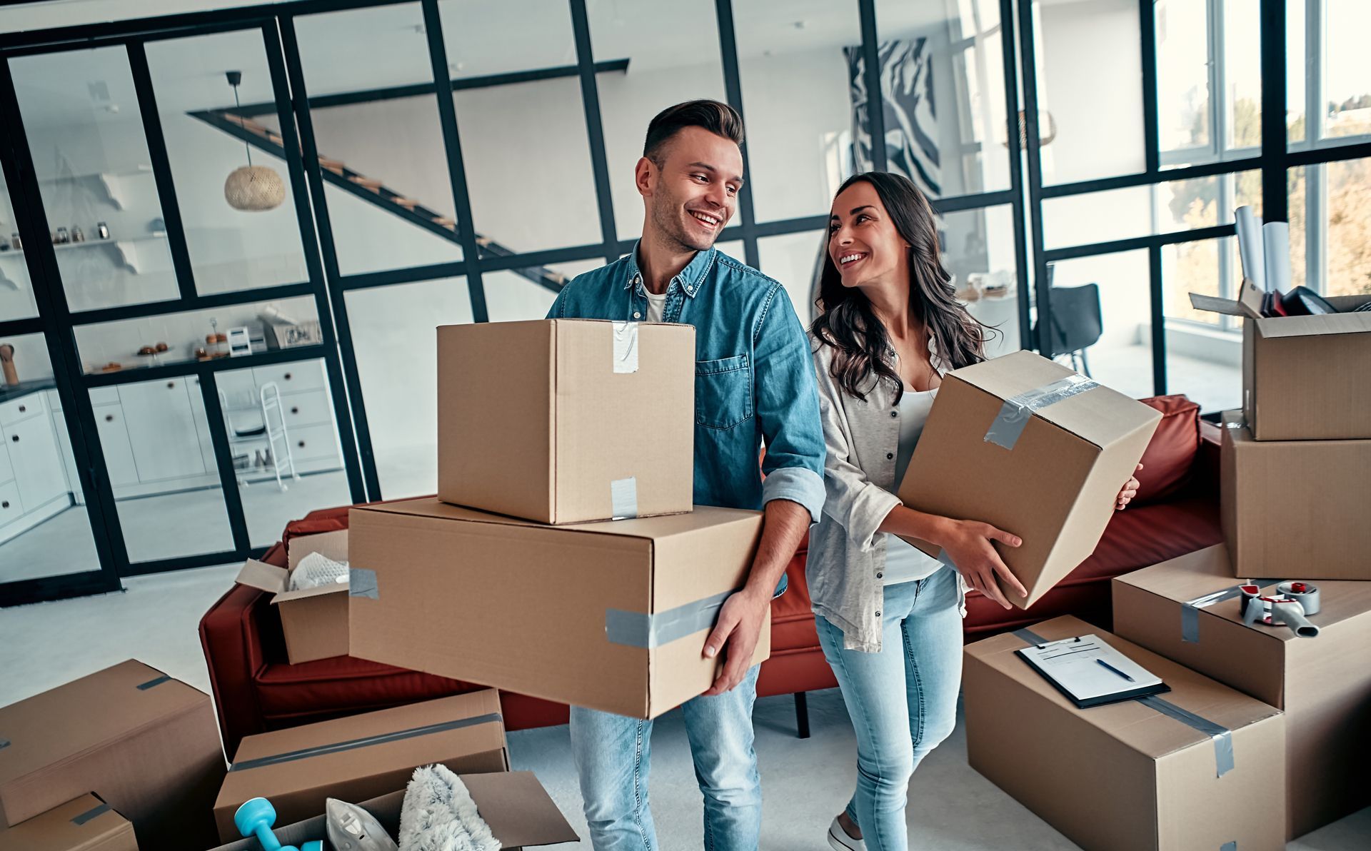 A man and a woman are holding cardboard boxes in a living room.