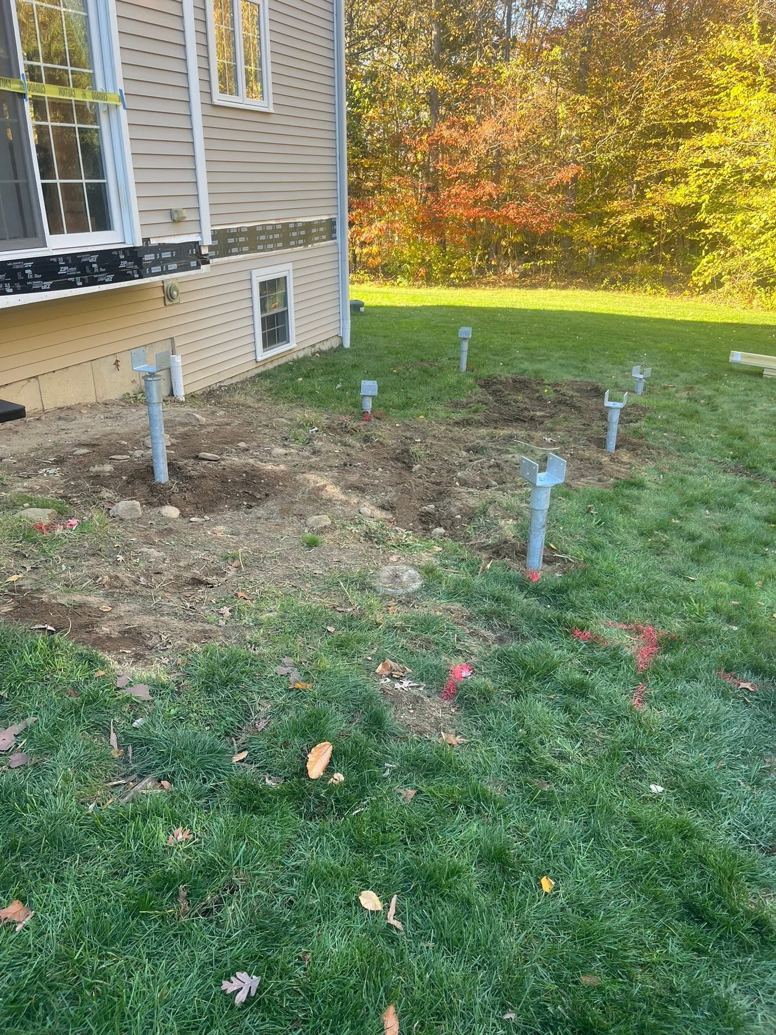 House side yard with newly marked utility pipes in soil and grass under autumn trees