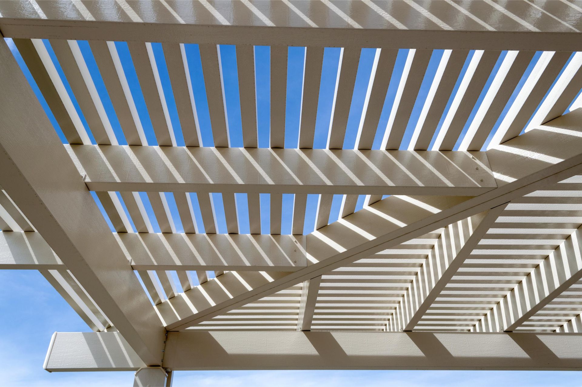White pergola beams casting striped shadows against a bright blue sky