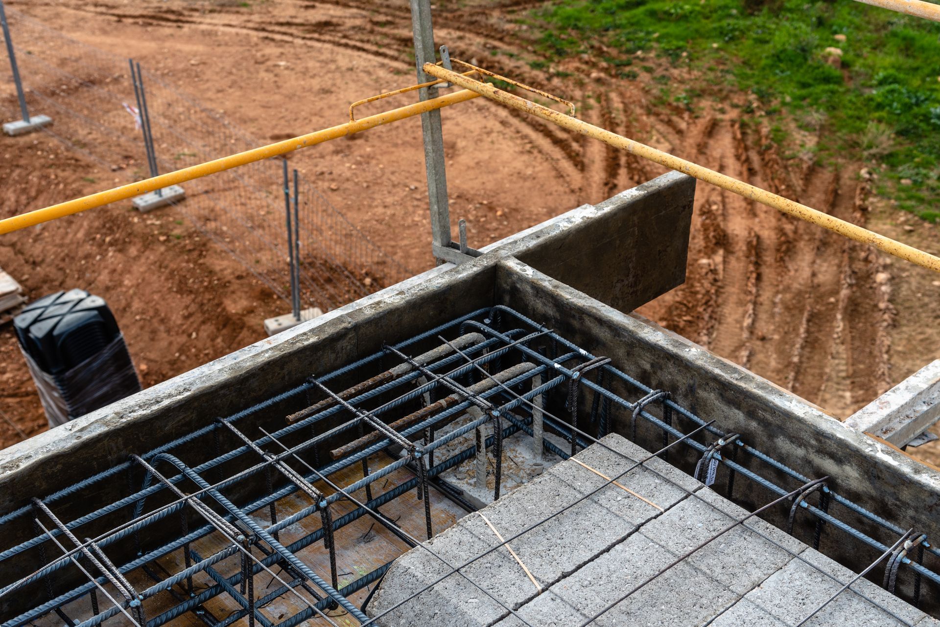 Concrete foundation under construction with steel rebar and a brick wall on a dirt site