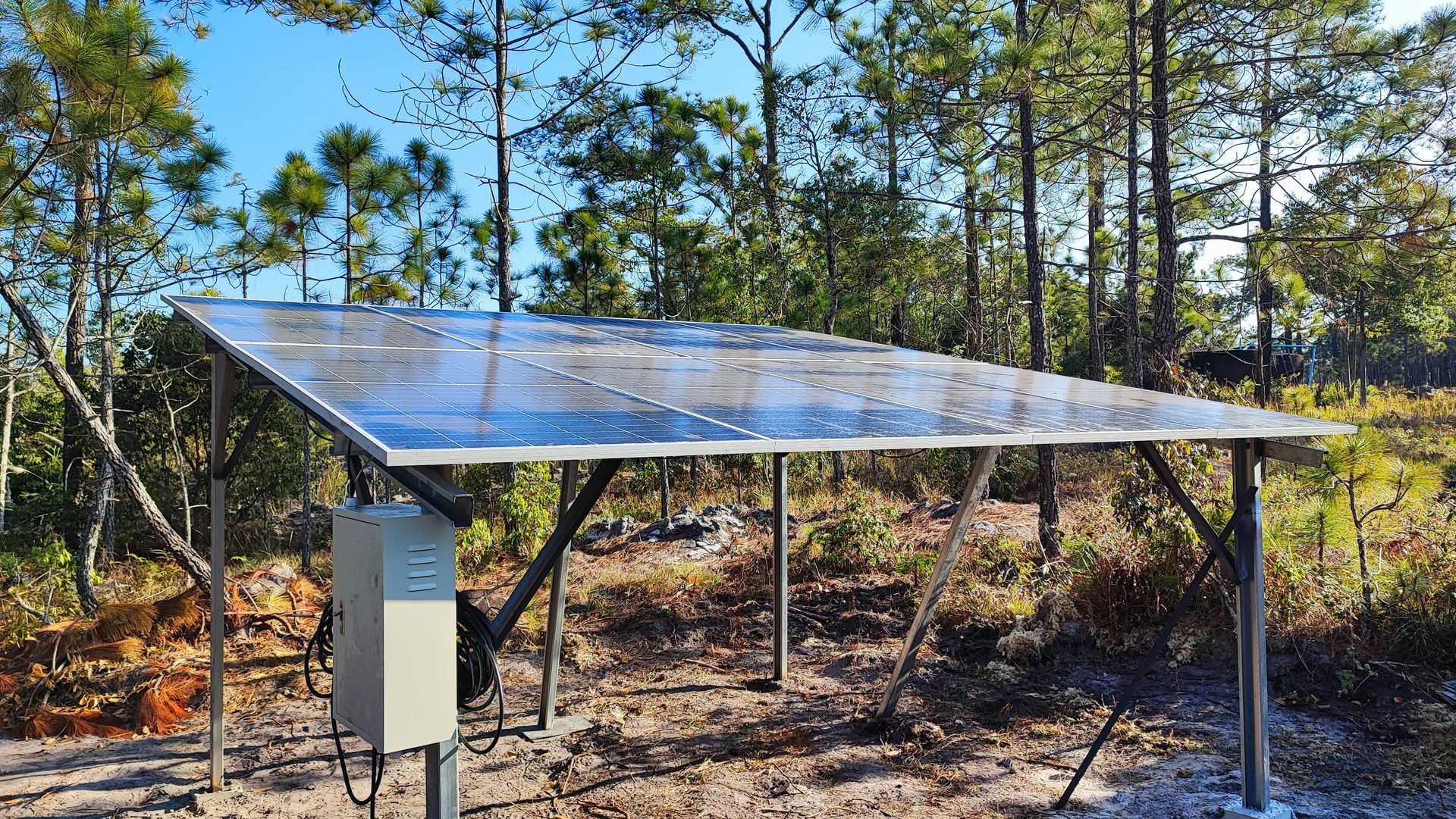 Solar panel array on a metal frame in a wooded clearing with a control box attached.