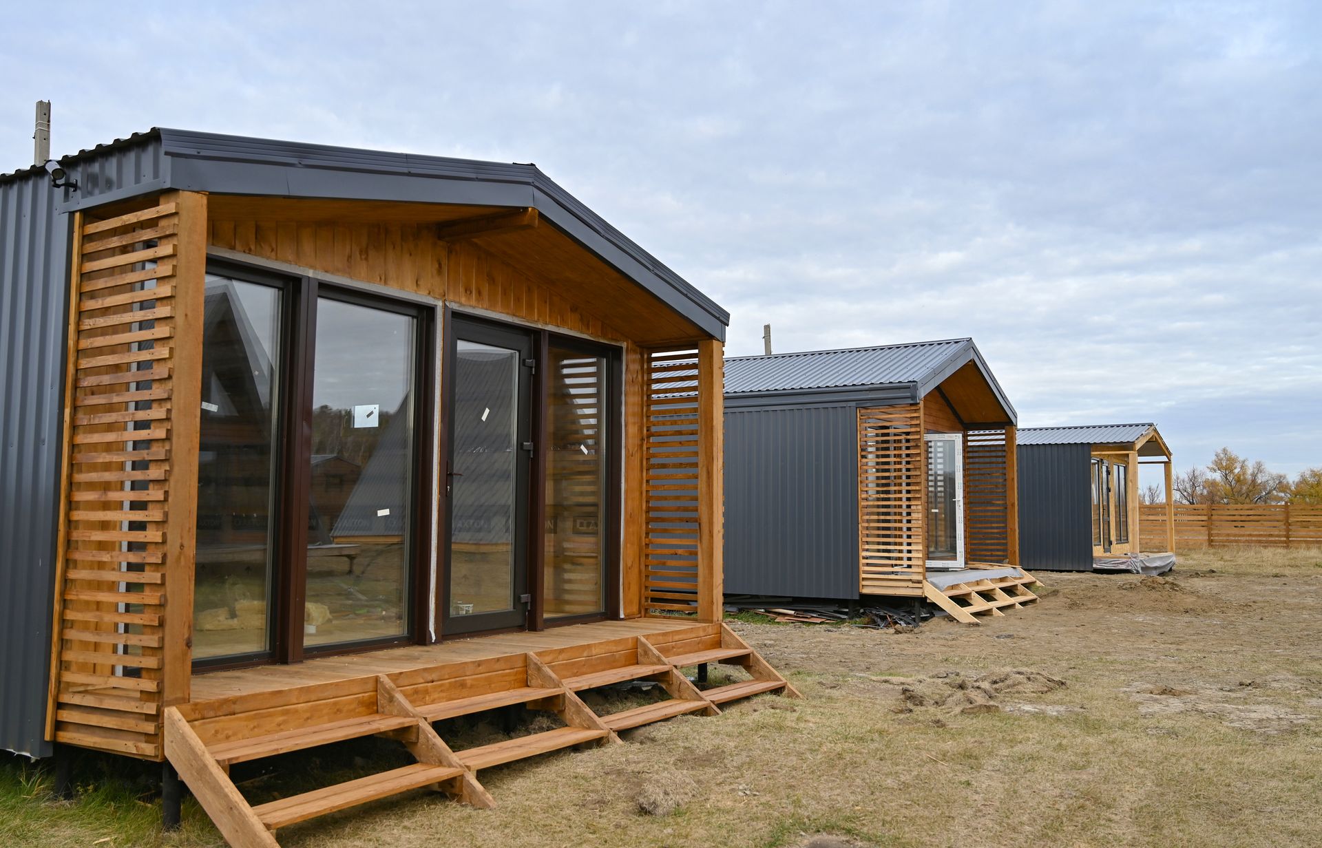 Tiny wood-clad cabins on a grassy field under a cloudy sky.