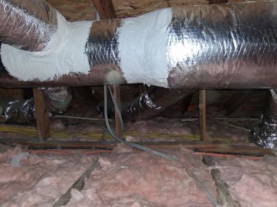 Attic view of metal air ducts with mastic sealant applied to joints, positioned above pink fiberglass insulation.