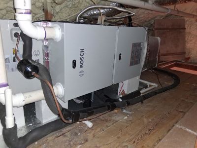 A gray Bosch air handler unit with attached piping and electrical conduits installed in an attic space.
