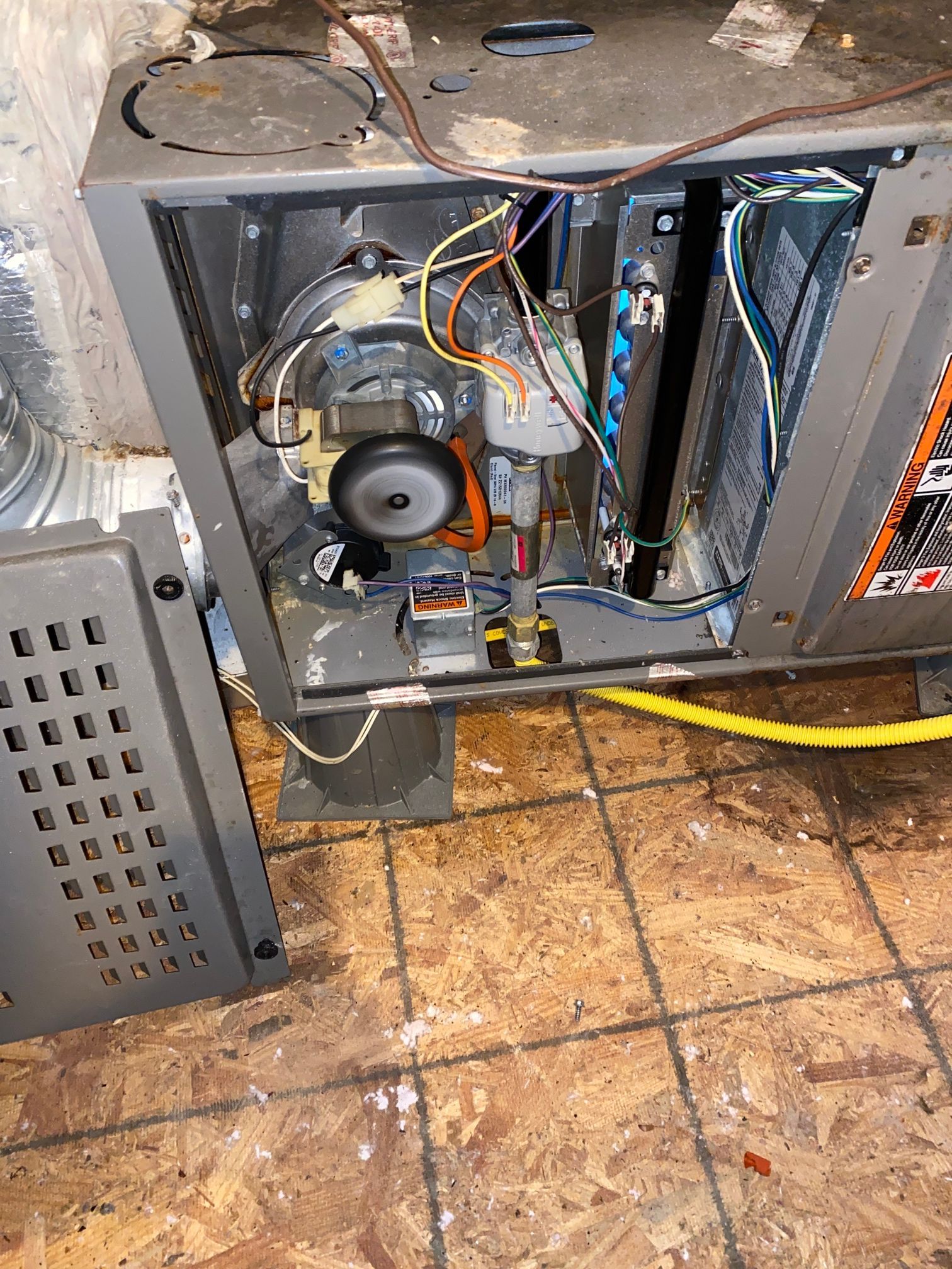The interior of an open grey residential furnace unit with exposed wiring, a motor, and a detached metal access panel.