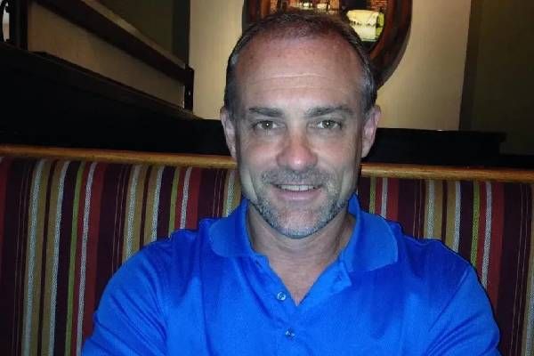 A smiling person in a blue polo shirt sits in a booth with vertical striped upholstery.