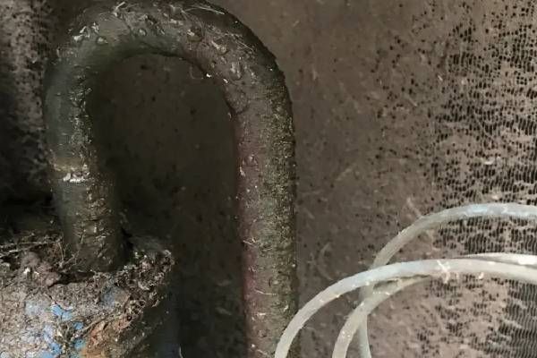 A U-shaped metal pipe coated in thick grime sits next to a coil of thin, translucent plastic tubing.