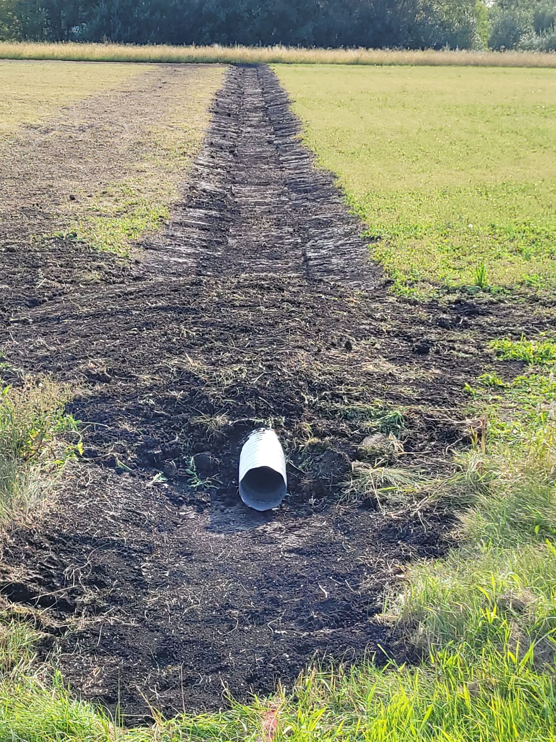 A white pipe is sitting in the middle of a dirt field.