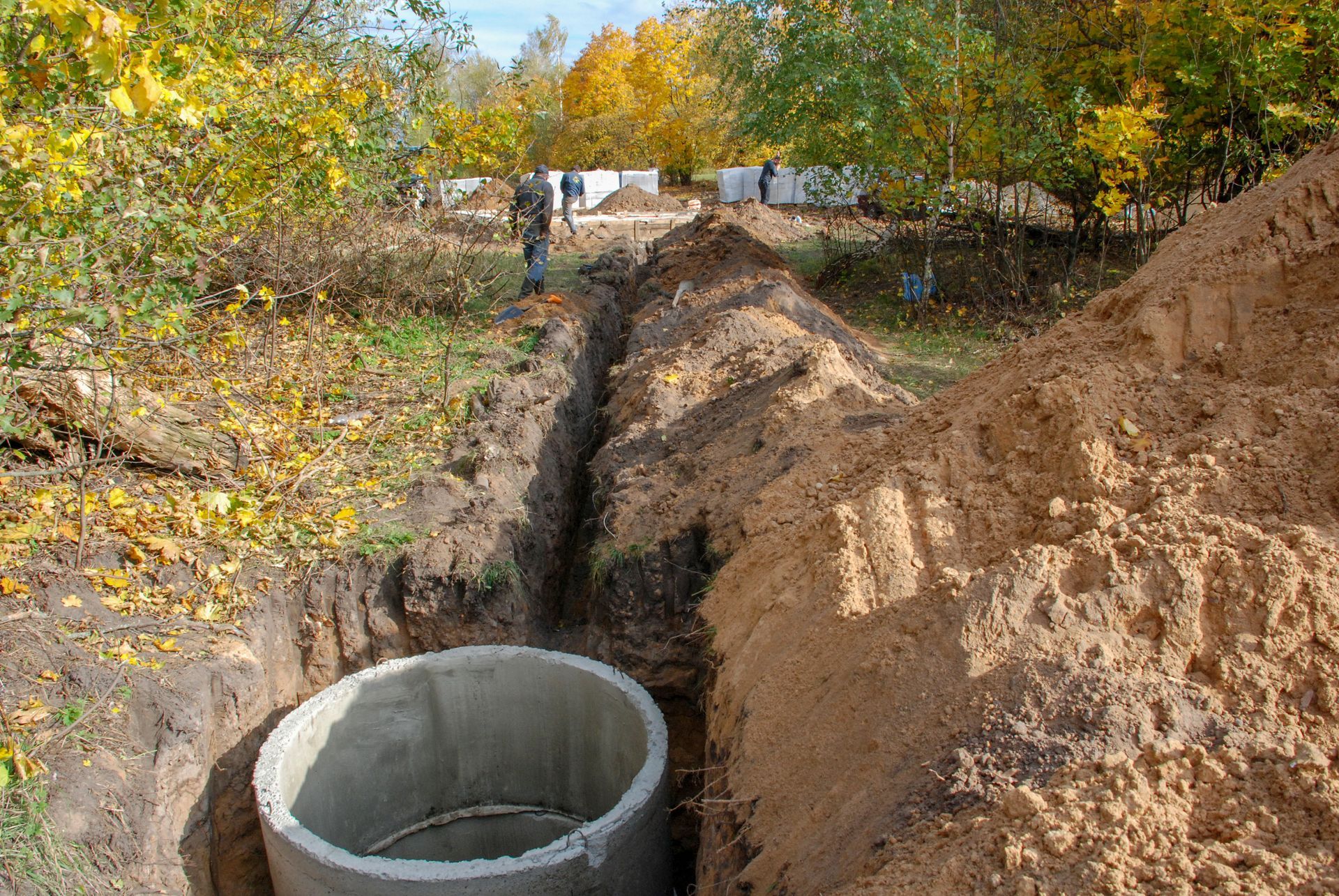 A concrete ring is sitting in the dirt next to a pile of dirt.
