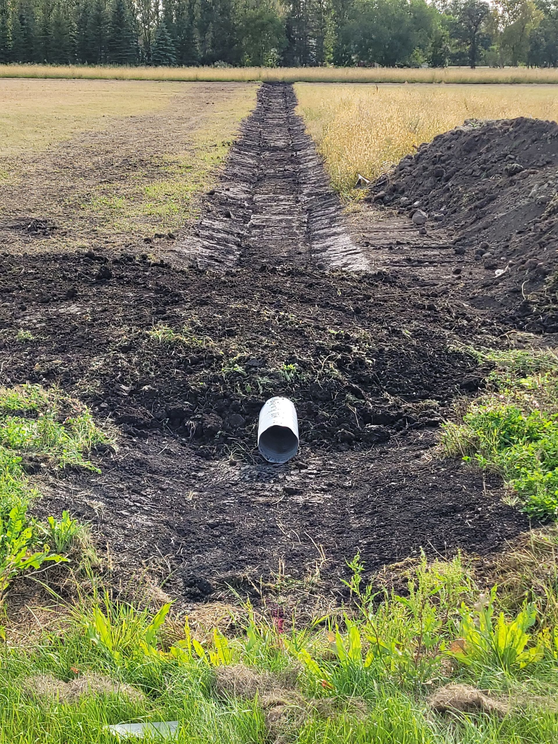 A white pipe is sitting in the middle of a muddy field.