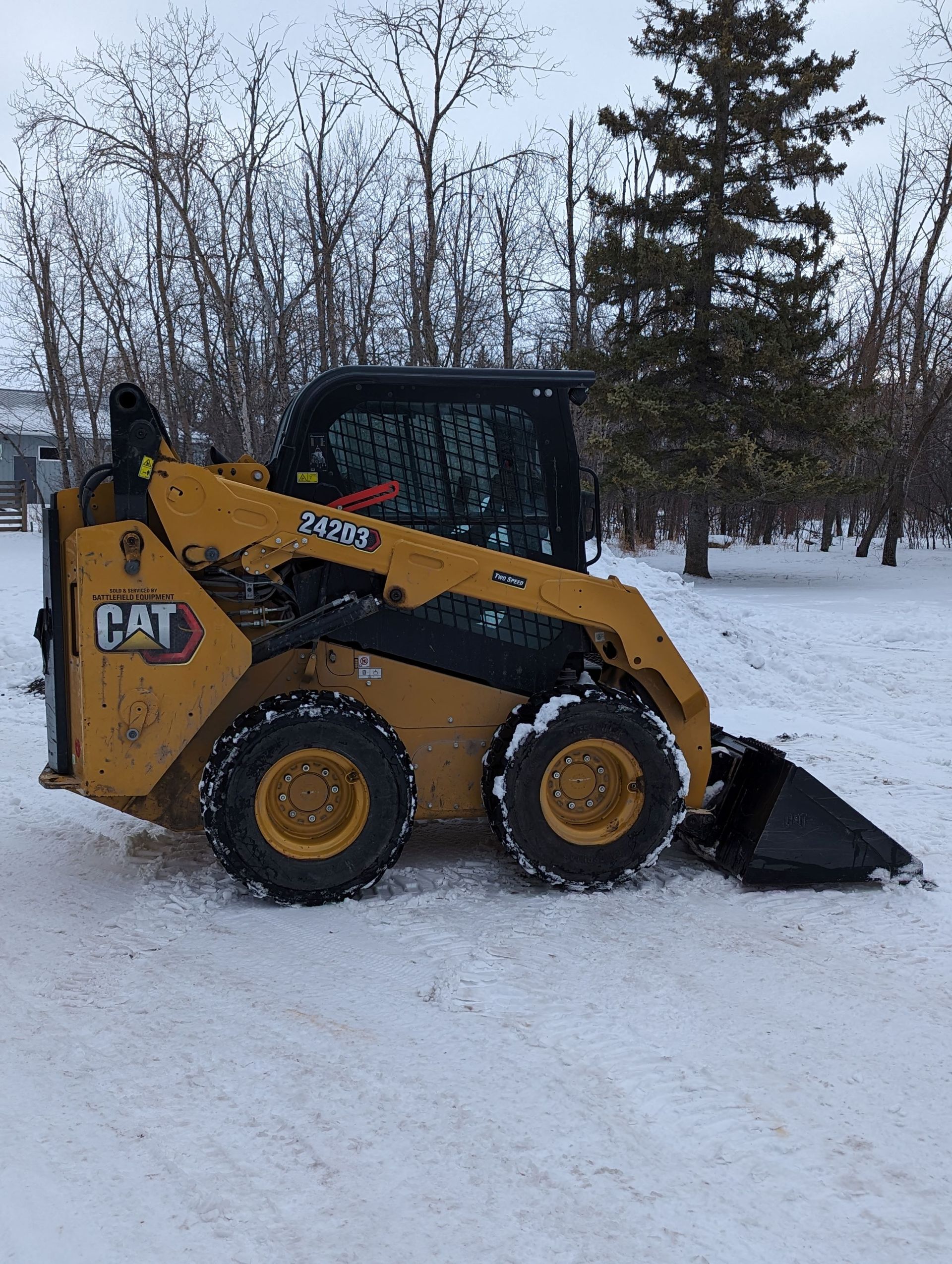 A yellow and black cat skid steer is parked in the snow.