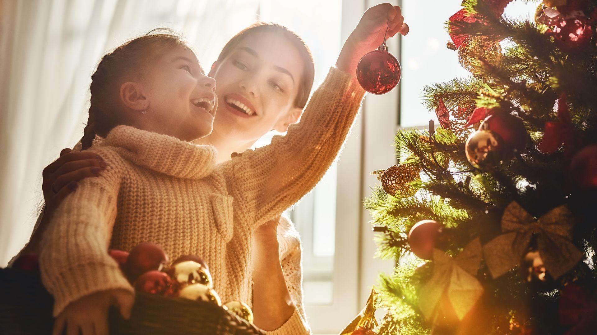 mother helping her daughter hang christmas ornaments