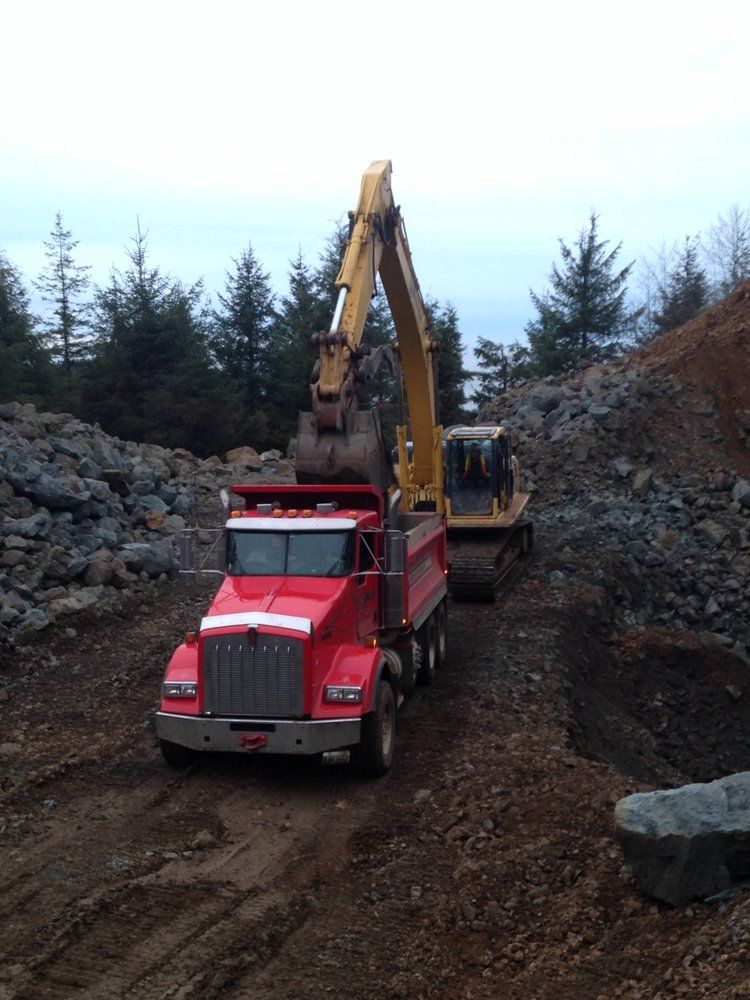 A red dump truck is being loaded with rocks by a yellow excavator