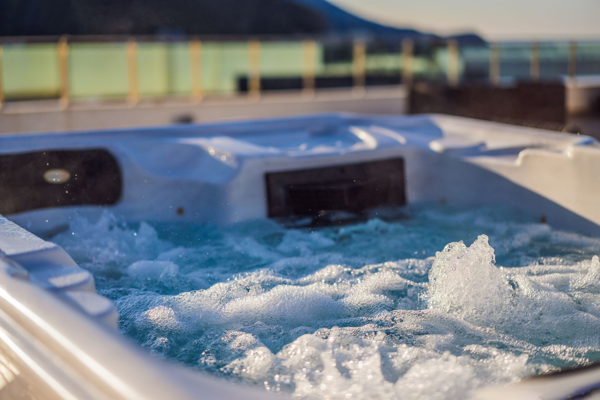 A hot tub filled with bubbling water on an outdoor deck overlooking a scenic coastline.