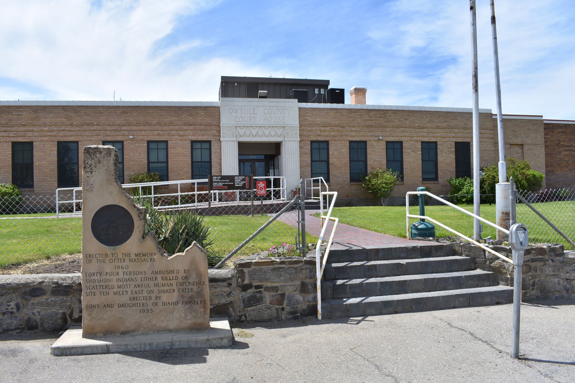 Stone monument in front of a brick building with a few steps and flags.