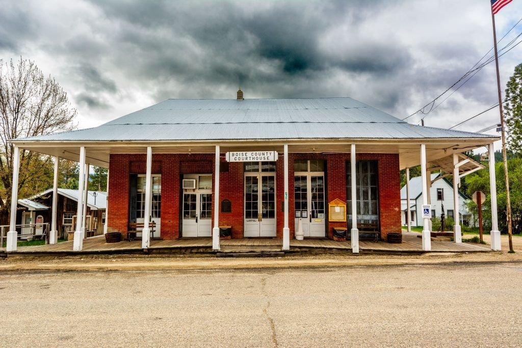 Red brick building with a white porch and corrugated metal roof under a cloudy sky.