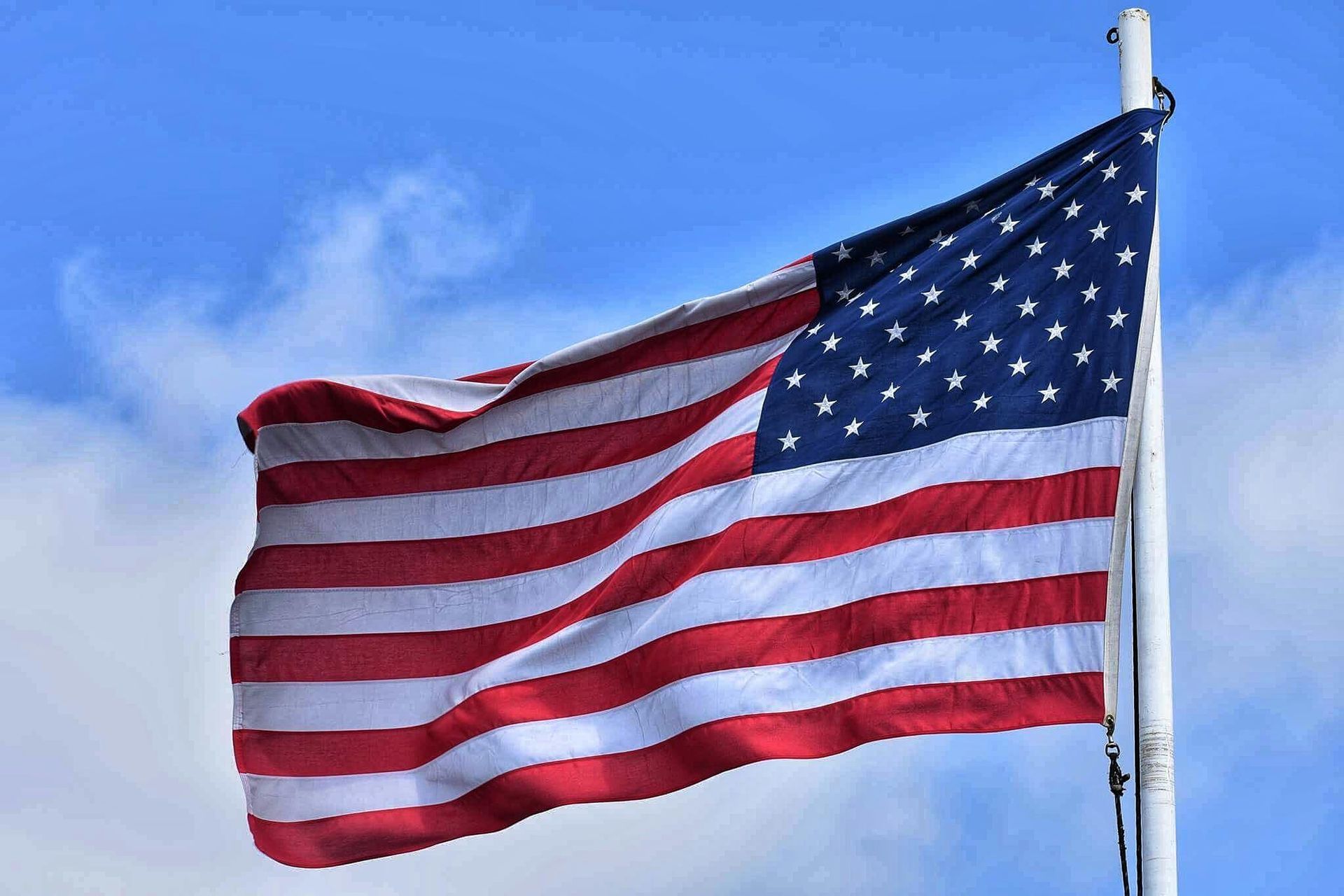 American flag waving in the wind against a blue sky, displaying red and white stripes and white stars.