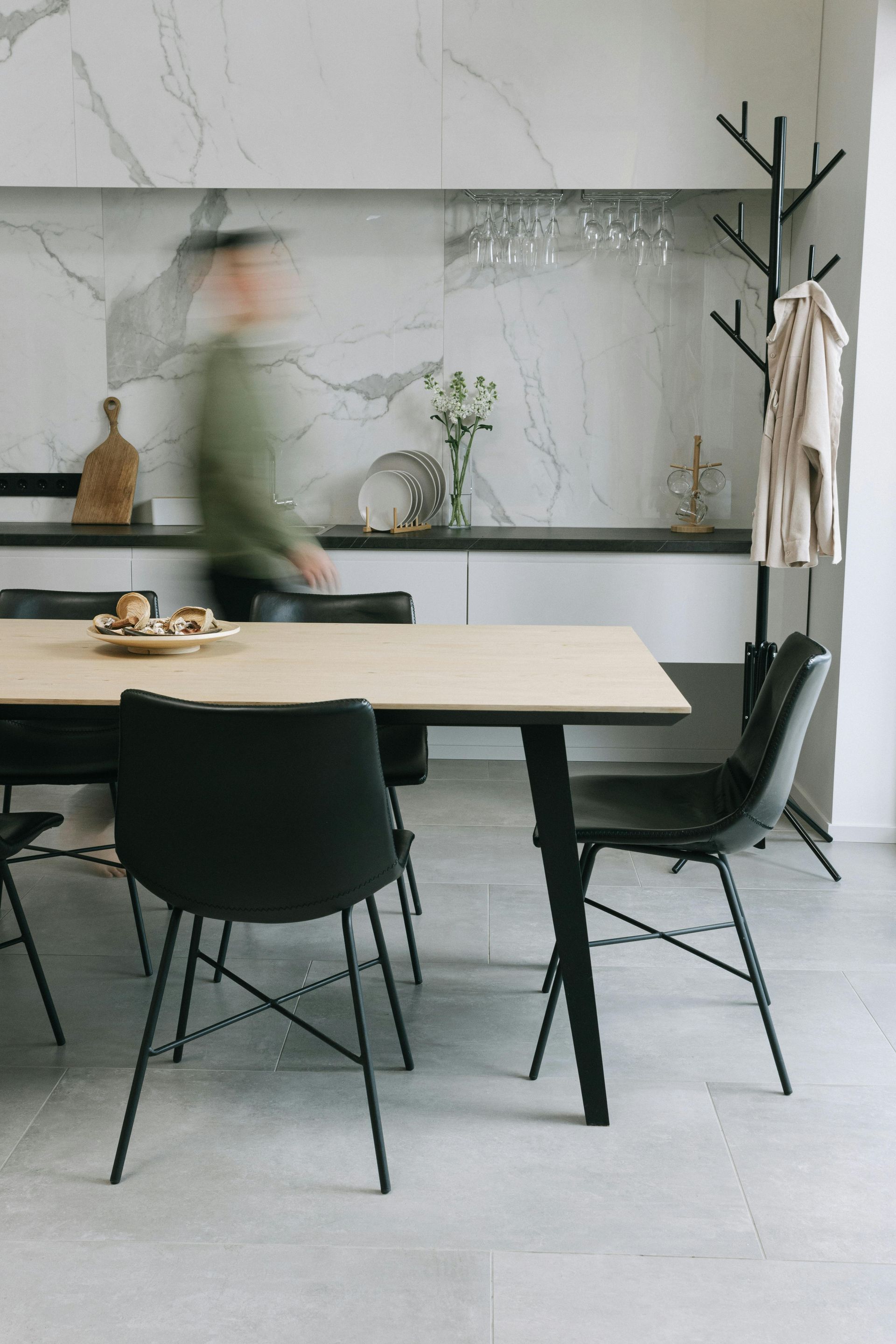 Blurred figure walking in a dining room with a table, black chairs, and a marble backsplash.