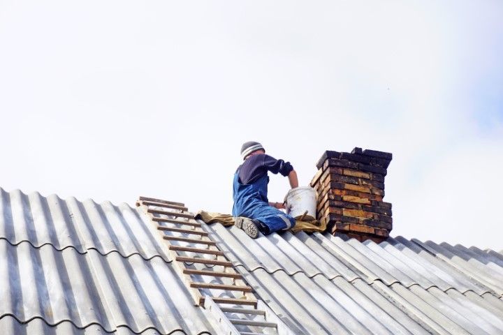 Worker repairing a corrugated roof beside a stack of bricks under a bright sky