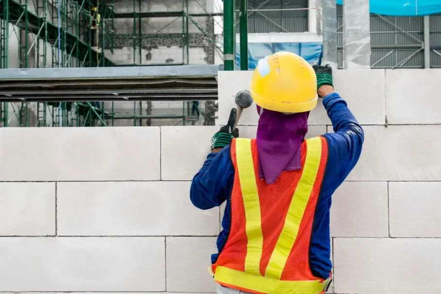 Construction worker in yellow hard hat and reflective vest building a cinder block wall