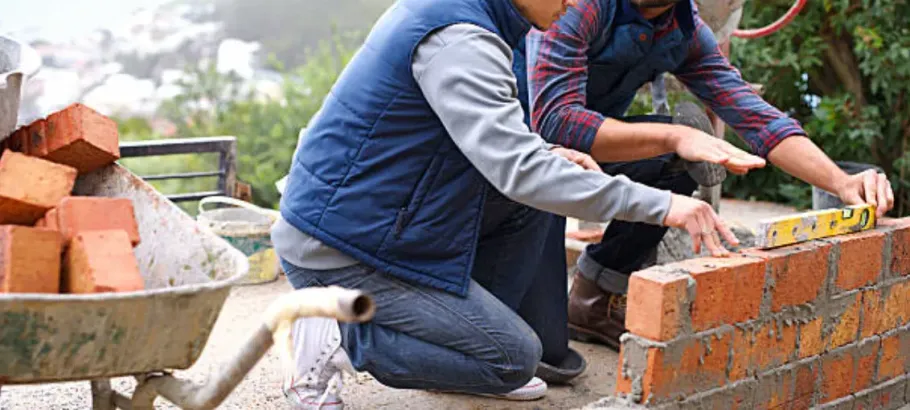 Workers laying red bricks to build a wall outdoors