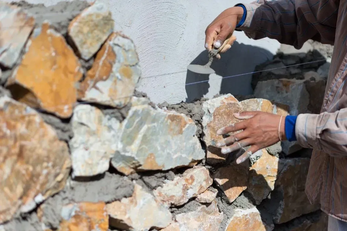 Hands placing stones into a rough stone wall during construction or repair