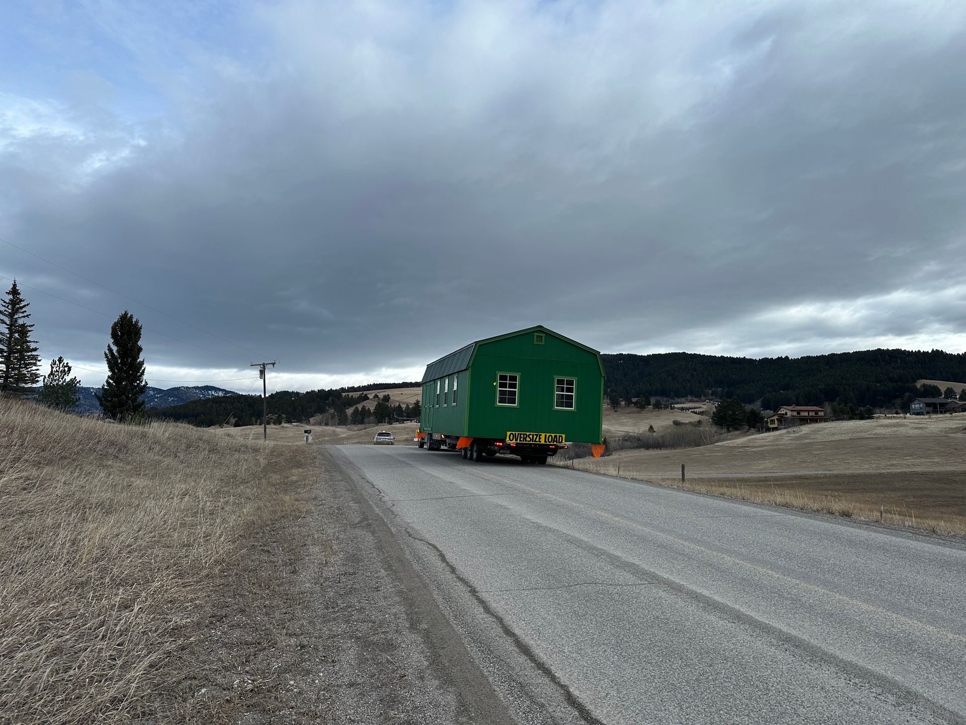 A tow truck is pulling a small house down a dirt road
