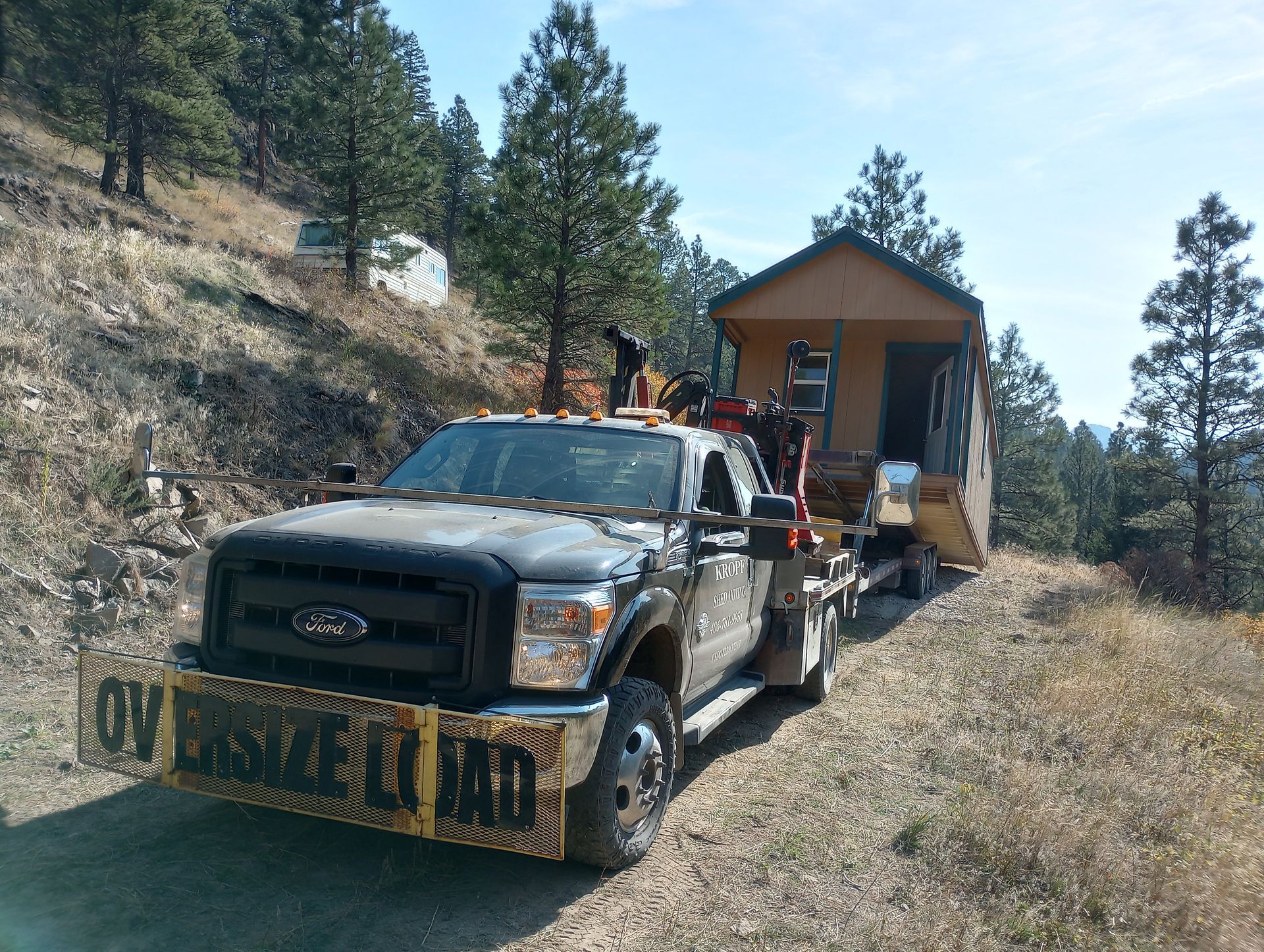 A tow truck is pulling a small house down a dirt road
