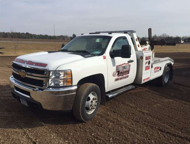 A white tow truck is parked in a dirt field.