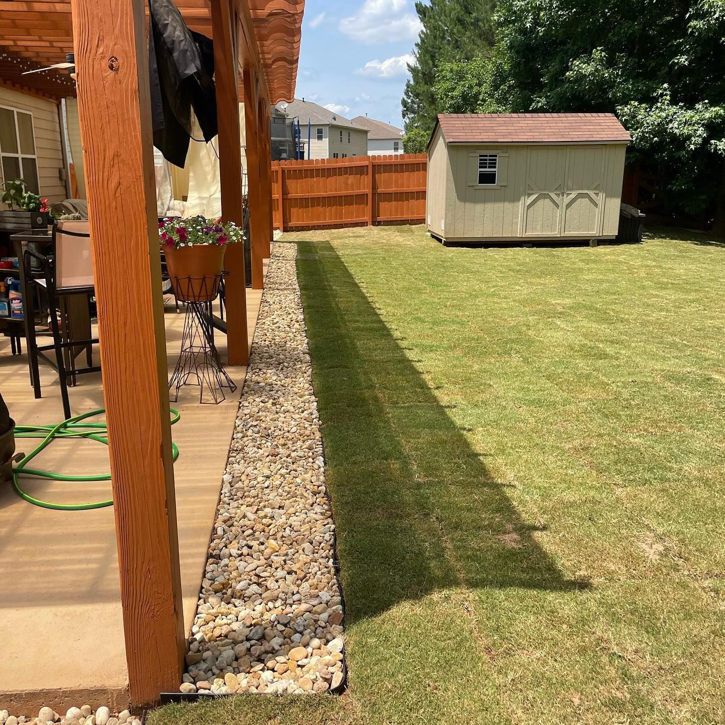 Backyard patio with wooden posts, gravel border, green lawn, fence, and a storage shed.