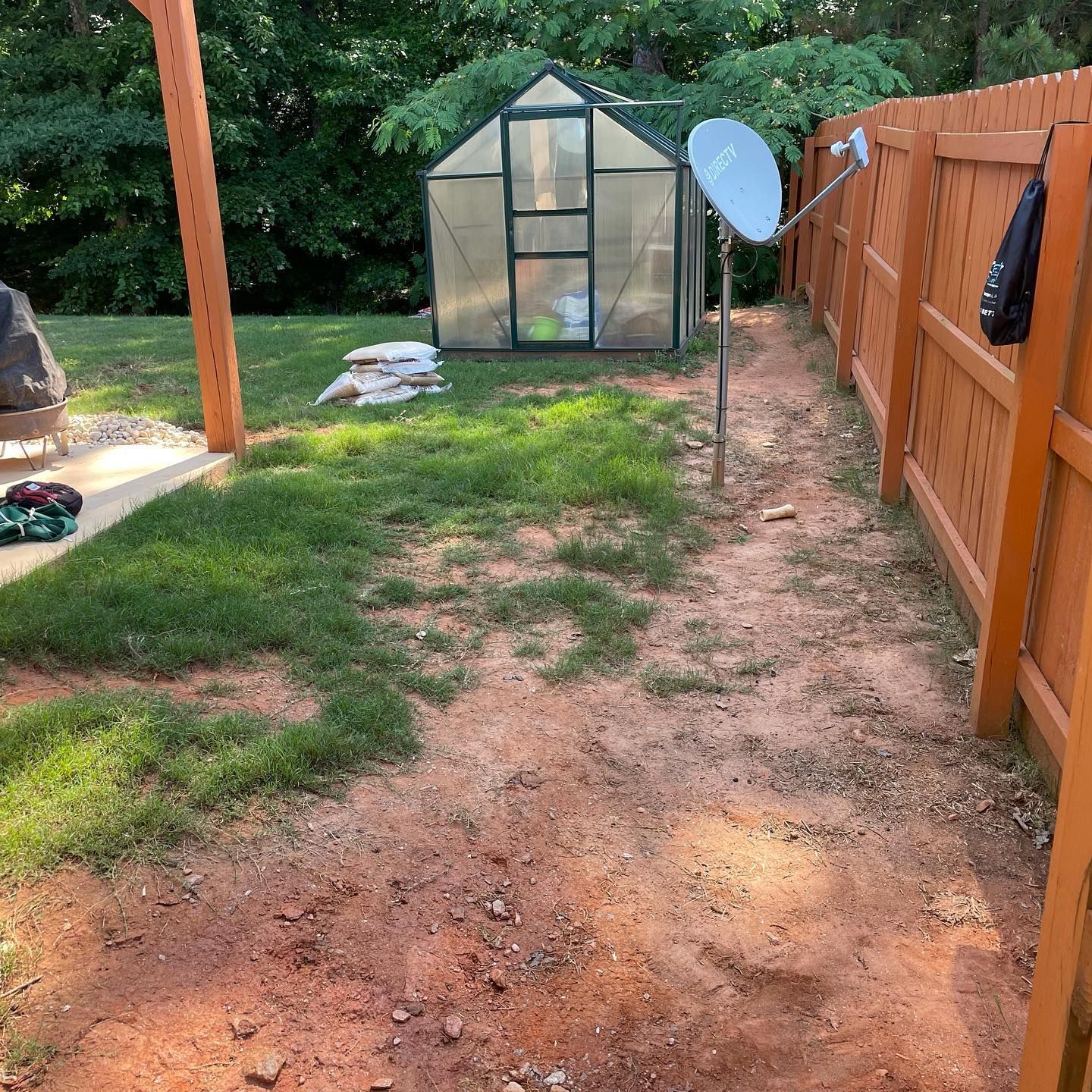 Backyard path with patchy grass, a greenhouse, wooden fence, and a satellite dish.