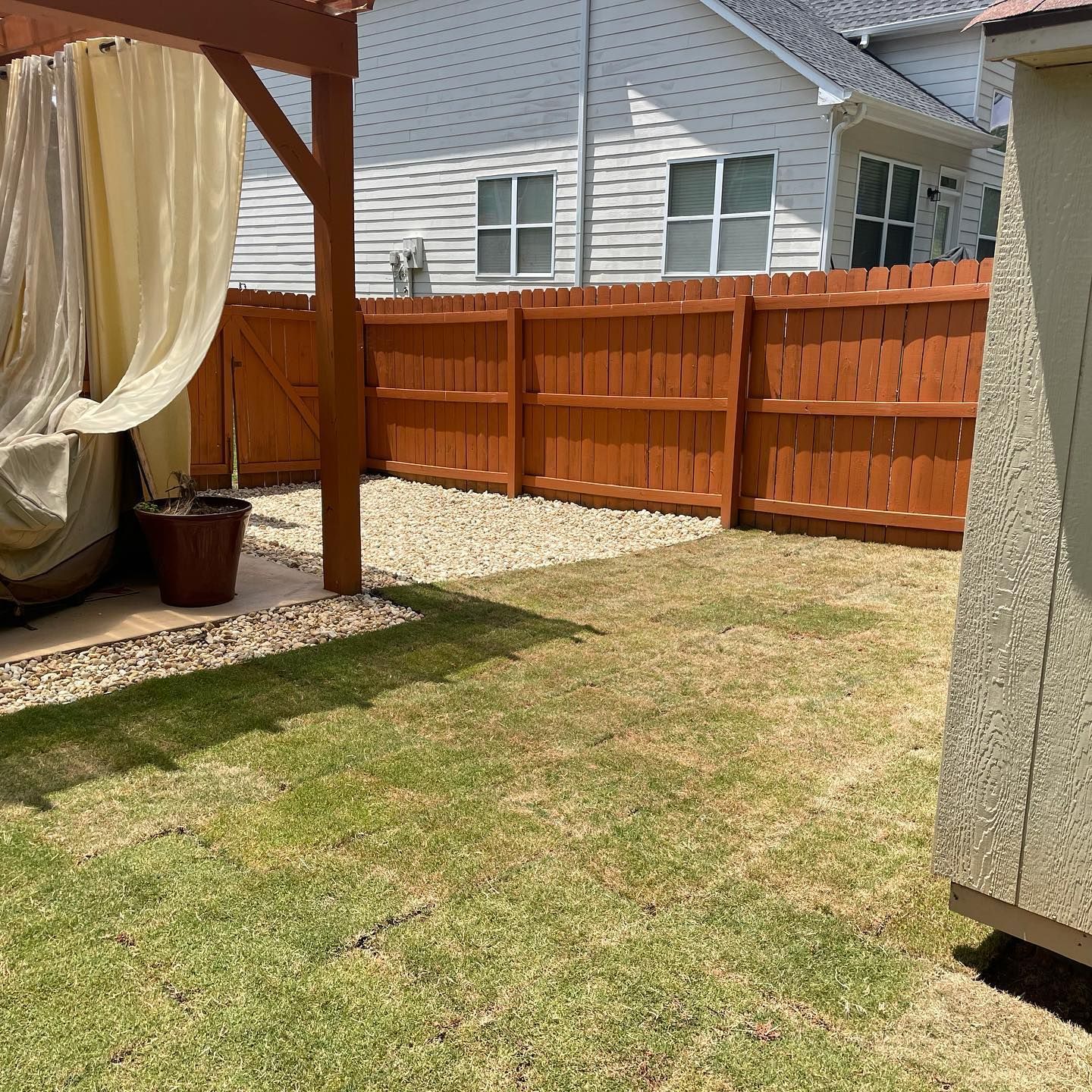Backyard patio with tan curtains, orange fence, grass lawn, and neighboring houses in the background