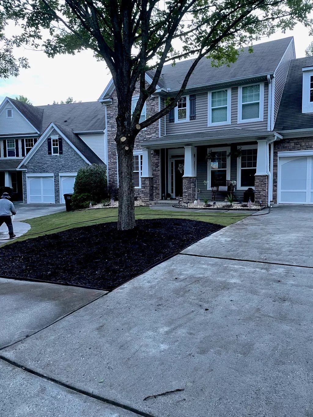 Suburban townhouse with driveway, front porch, and a large tree in the front yard.