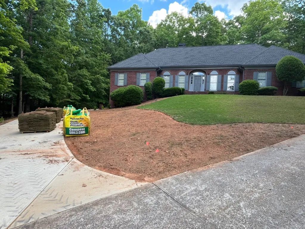 Front yard landscaping with fresh mulch, a driveway, and a brick house surrounded by trees.
