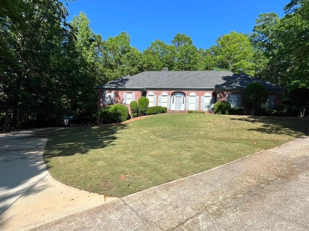 Single-story brick house with white shutters, a large front lawn, and curved driveway under sunny blue sky