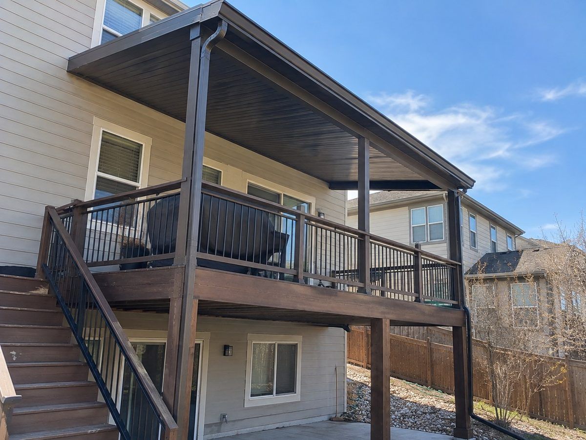 Brown aluminum patio cover over an elevated deck with black railings, built by Colorado Outdoor Builders