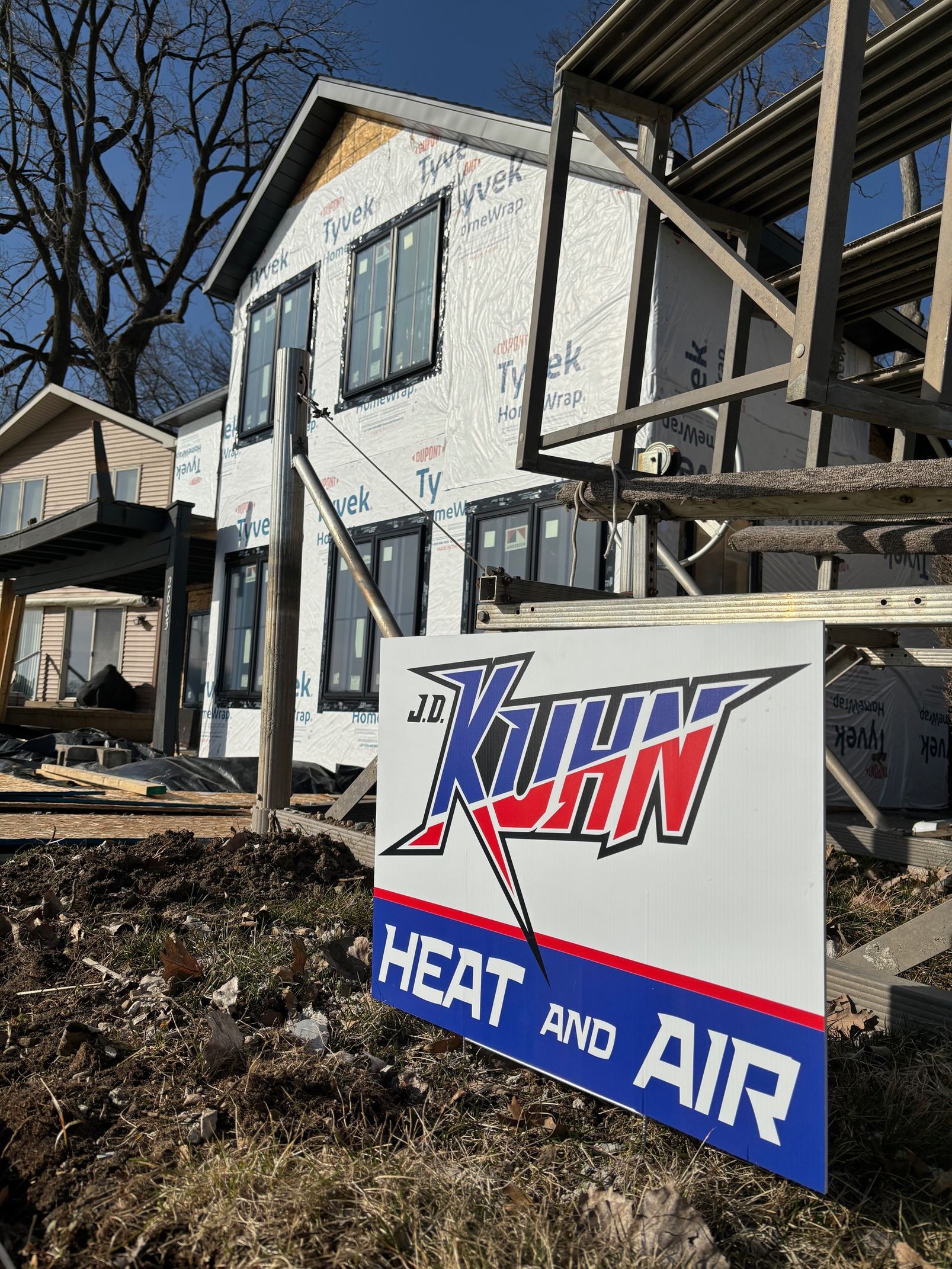 A sign for john heat and air is in front of a house under construction.