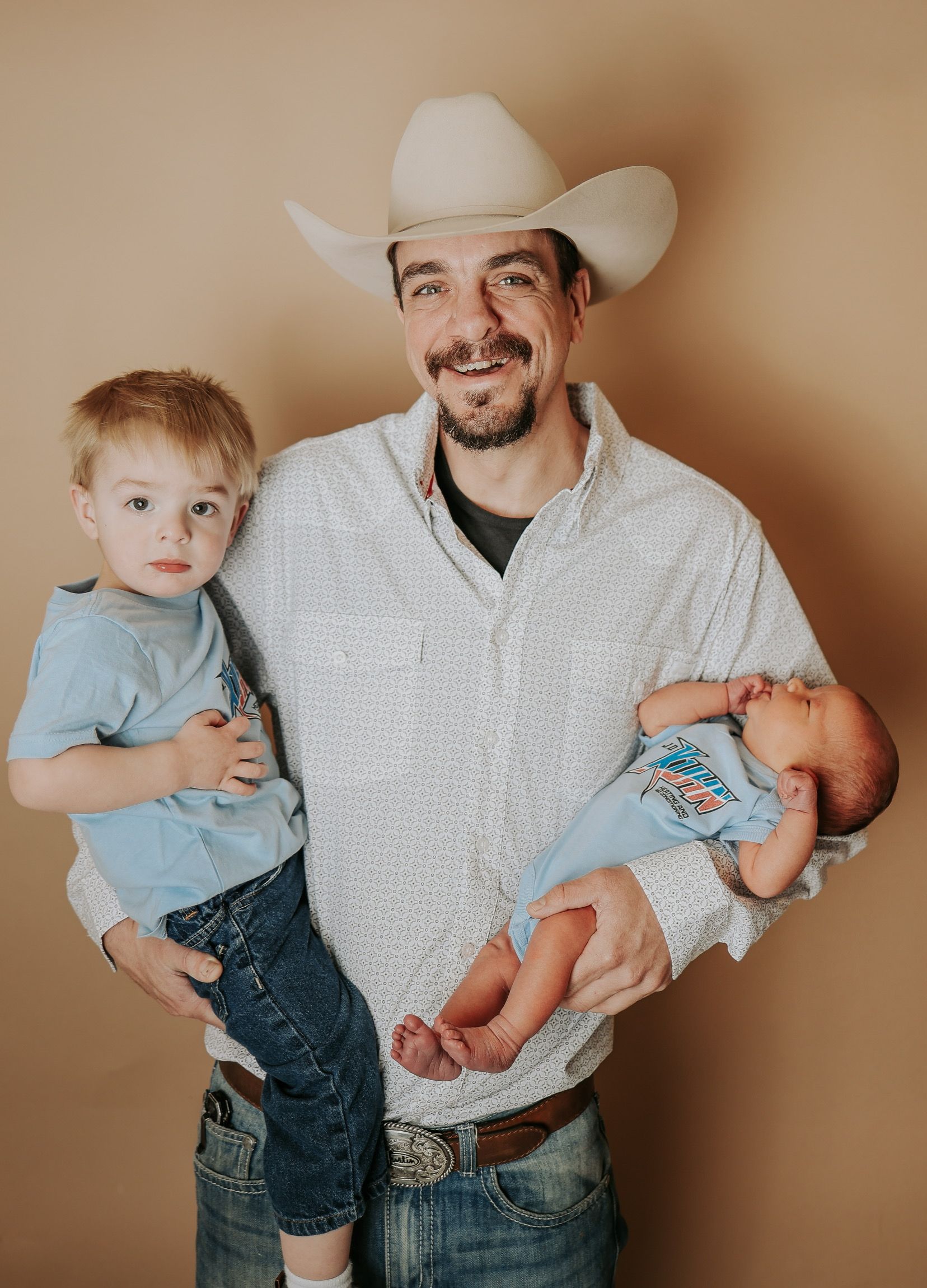 A man in a cowboy hat is holding two children.